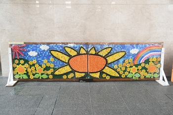 写真：ペットボトルキャップアート（ペットボトルのキャップで青空、太陽、虹、ひまわり畑が表現されています）