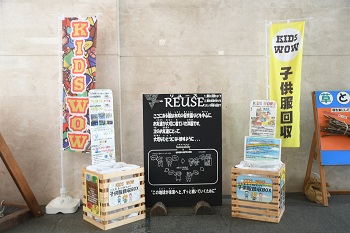 写真：「KIDS WOW　子供服回収」と書かれた旗が立っており、子供服回収ボックスやリユースに関する立て看板が立っています