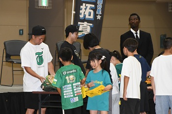 写真：会場内に飾られていたベルトを実際に手に取る子どもたちと、それを見守るいのうえなおや選手といのうえたくま選手