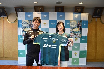 むとう選手と市長がむとう選手の直筆サインを入れたユニフォームのレプリカを掲げる様子